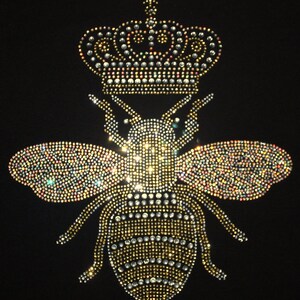 Peut inclure: Une abeille en strass dor&eacute;e et argent&eacute;e avec une couronne sur la t&ecirc;te. L'abeille est sur un fond noir.