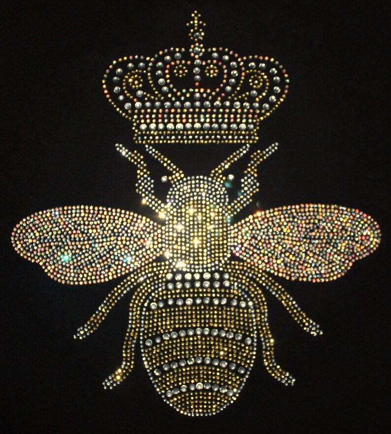 Peut inclure: Une abeille en strass dor&eacute;e et argent&eacute;e avec une couronne sur la t&ecirc;te. L'abeille est sur un fond noir.