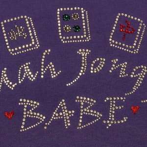 May include: Purple shirt with the words "Main Squeeze Babe" in silver rhinestones. There are four red and silver dice designs on the shirt.