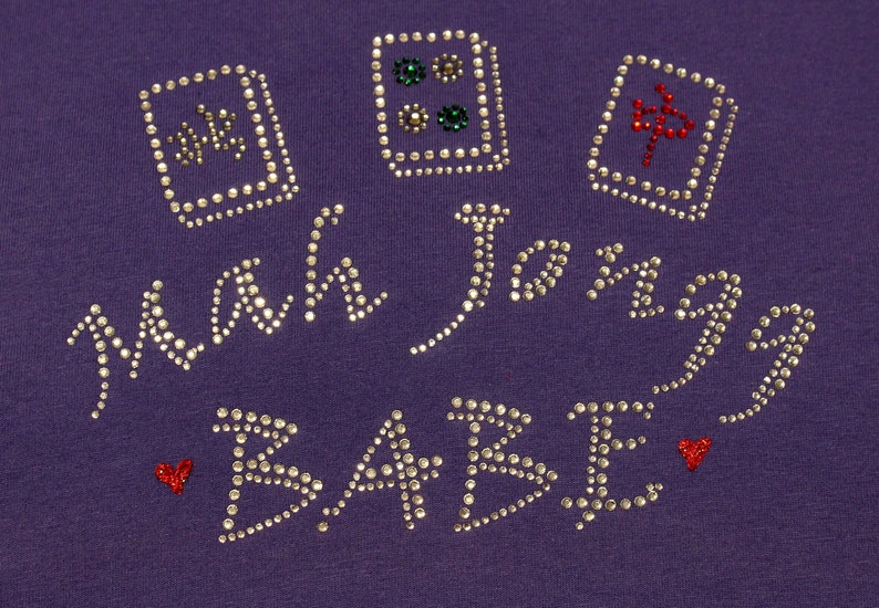 May include: Purple shirt with the words "Main Squeeze Babe" in silver rhinestones. There are four red and silver dice designs on the shirt.