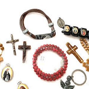 May include: Assortment of religious jewelry and accessories, including wooden rosaries, crucifixes, a leather bracelet with a metal charm, a black bracelet with religious icons, a red wooden rosary, a wooden cross keychain, a small metal angel keychain, and a white card with the text "Gracias con Pope".