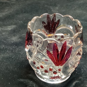 Op de afbeelding: Een glazen kaarsenhouder met een gegolfde rand en een rood bloemenontwerp.