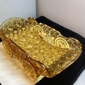 Könnte beinhalten: Ein dekoratives, bernsteinfarbenes Serviertablett aus Glas in Form eines Oldtimers. Das Tablett weist ein detailliertes Sternmuster und Raddesigns auf, die einen Hauch von Retro-Charme verleihen. Das Tablett ist etwa 30 cm lang.