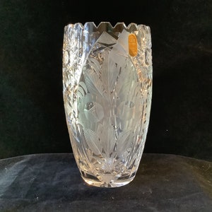 May include: A clear glass vase with a cut crystal design. The vase has a scalloped rim and is etched with a floral pattern.