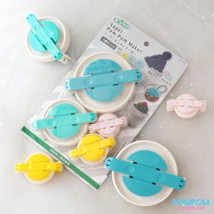 May include: A set of four Clover Super Pom-Pom Makers in different sizes. The makers are white with blue, pink, and yellow accents. The packaging includes the text "Super Pom-Pom Maker" and "4個セット".
