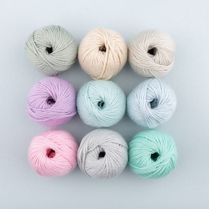May include: Nine balls of yarn in various pastel colours, including light blue, light green, pink, purple, and cream. The balls of yarn are arranged in a square pattern on a light blue background.