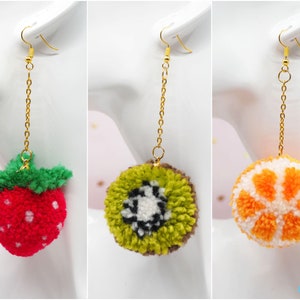 May include: Three pairs of fruit-themed dangle earrings. The earrings feature a strawberry, a kiwi, and an orange. The fruit is made of yarn and is attached to a gold chain.