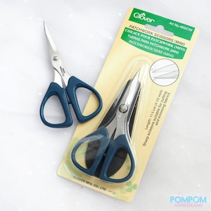 May include: Two pairs of Clover Patchwork Scissors (Mini) with blue handles. One pair is loose, and the other is in its original packaging. The packaging is light green and yellow, with text in multiple languages. The scissors are 11.5 cm long.