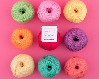 May include: Ten balls of yarn in different colors, including pink, yellow, orange, green, and purple. The balls are arranged in a circle on a pink background. A white label with the text "YARN AND COLORS. MUST-HAVE MINI" is in the center of the circle.