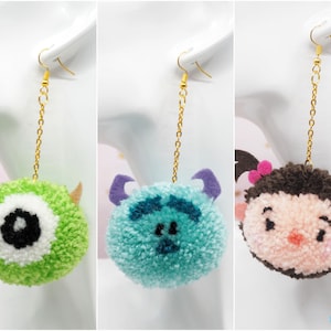 Puede incluir: Tres pares de pendientes colgantes con personajes de películas de animación populares. El primer par presenta un monstruo verde con un ojo grande, el segundo par presenta un monstruo azul con dos ojos y el tercer par presenta un personaje marrón con mejillas rosadas y un lazo rosa.