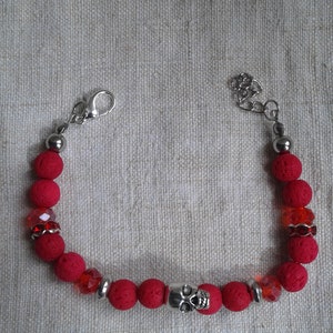 Peut inclure: Bracelet en perles de roche volcanique rouge avec un charme de crâne argenté et des accents de cristal rouge transparent.