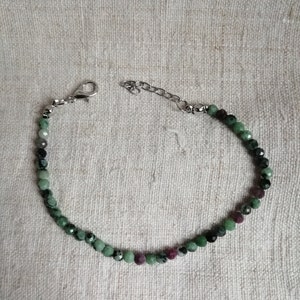 Op de afbeelding: Een groene en zwarte edelsteen armband met een zilveren sluiting. De armband is gemaakt van kleine, ronde kralen.