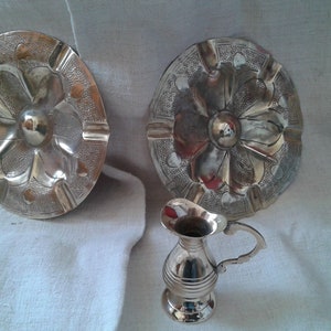 Puede incluir: Dos bandejas decorativas de plata con un diseño floral y una pequeña jarra de plata.