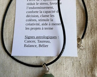 May include: Aventurine gemstone pendant necklace on a black cord. The pendant is a light green, oval-shaped stone. The card reads: "Aventurine Pierre de l'apaisement, réduit le stress, favorse l'endormissement, conforte la capacité de décision, clame les colères, stimule la créativité, aide à mener les projets à terme Signes astrologiques: Cancer, Taureau, Balance, Bélier"