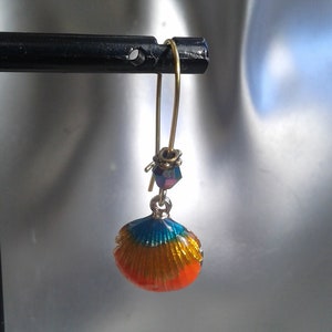 Peut inclure: Une paire de boucles d'oreilles pendantes dorées avec un charme coquillage bleu, jaune et orange et une petite perle de cristal irisée.