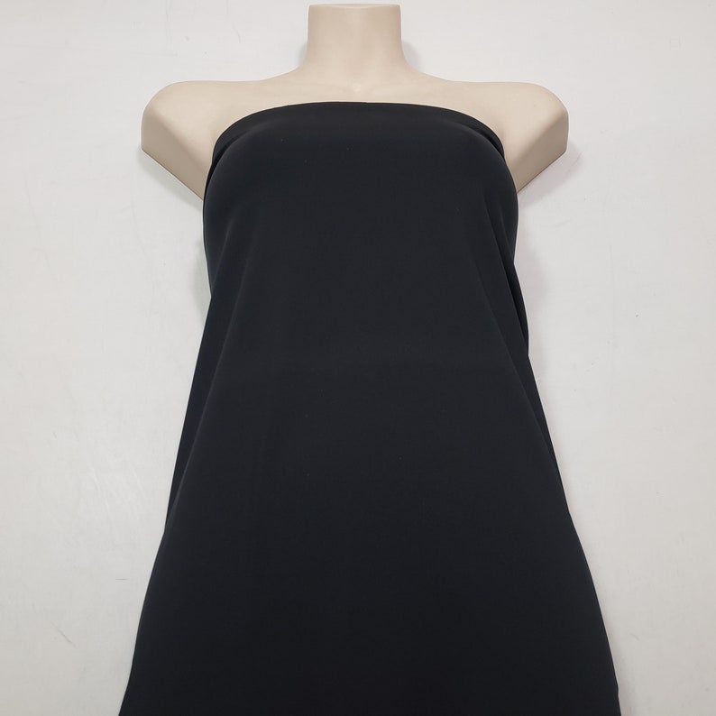May include: A black fabric draped over a mannequin. The fabric is smooth and appears to be a solid color. The mannequin is a neutral skin tone, and the background is a plain white.