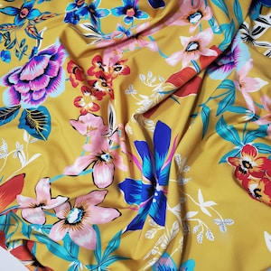 May include: Yellow fabric with a floral print featuring pink, blue, and red flowers. The fabric has a soft, flowing texture.