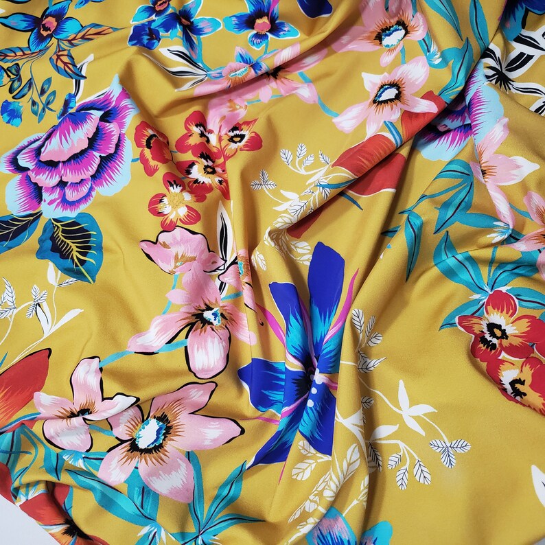 May include: Yellow fabric with a floral print featuring pink, blue, and red flowers. The fabric has a soft, flowing texture.