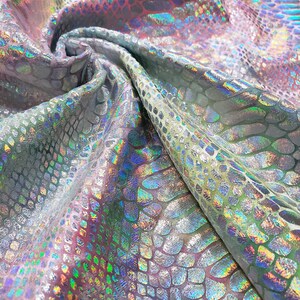 Puede incluir: Primer plano de una tela iridiscente con un patrón de piel de serpiente en tonos de verde, azul y rosa.