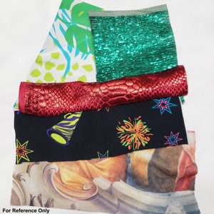 May include: A stack of fabric scraps in various patterns and colors, including green, red, black, and white. The fabrics include a sparkly green fabric, a red fabric with a snake skin pattern, a black fabric with a neon green and orange design, and a white fabric with a green and blue pattern.