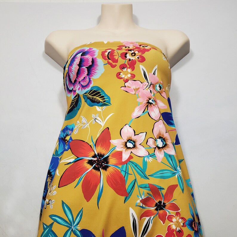 May include: A yellow strapless dress with a floral print featuring pink, red, blue, and green flowers. The dress has a fitted bodice and a flowing skirt.