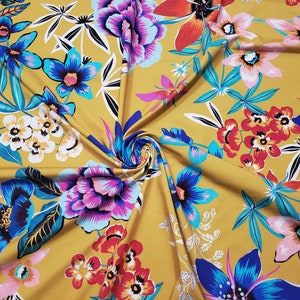 May include: Mustard yellow fabric with a floral print featuring various flowers in shades of pink, blue, red, and white. The fabric has a soft, flowing texture.