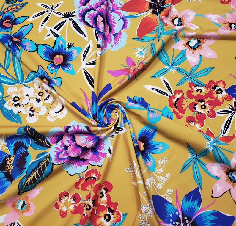 May include: Mustard yellow fabric with a floral print featuring various flowers in shades of pink, blue, red, and white. The fabric has a soft, flowing texture.