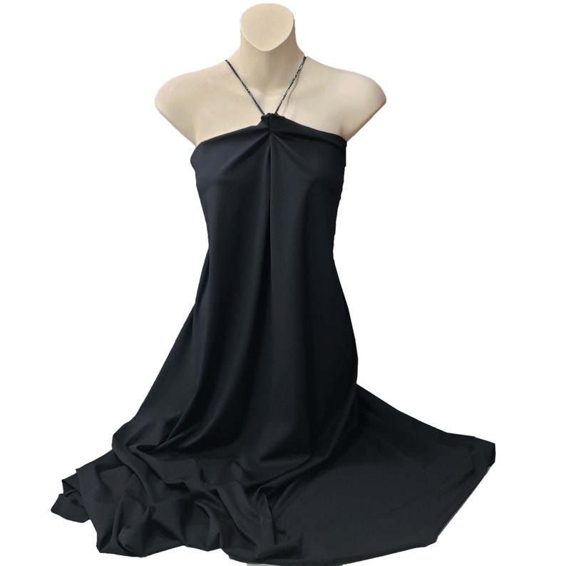 May include: A black halter dress displayed on a mannequin. The dress is made of a smooth, flowing fabric and features a halter neckline. A delicate necklace adorns the neckline. The dress drapes down, creating soft folds and a subtle train.