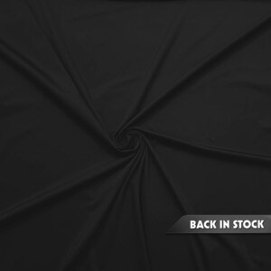 May include: A close-up of a black fabric with a smooth texture, swirled in the center. The fabric is draped, creating folds and shadows. The words "BACK IN STOCK" are displayed on a black banner in the lower right corner.
