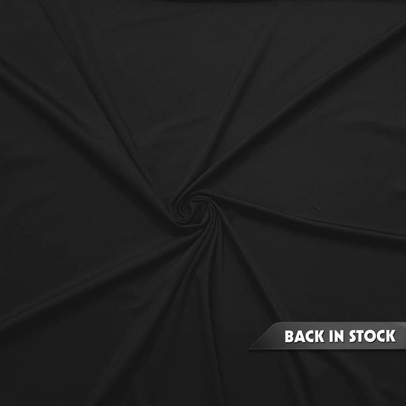 May include: A close-up of a black fabric with a smooth texture, swirled in the center. The fabric is draped, creating folds and shadows. The words "BACK IN STOCK" are displayed on a black banner in the lower right corner.