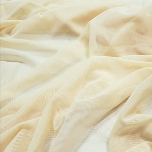 Pu&ograve; includere: Un primo piano di un tessuto a rete beige con una trama fine e uniforme. Il tessuto &egrave; morbido e cade bene, rendendolo ideale per una variet&agrave; di progetti di artigianato.