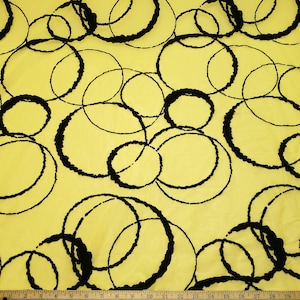 May include: Yellow fabric with a repeating pattern of black, imperfect circles. The circles vary in size and overlap, creating a dynamic and textured design. The fabric has a subtle sheen.