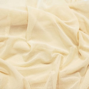 Pu&ograve; includere: Un primo piano di un tessuto color crema, trasparente, con una trama tessuta. Il tessuto &egrave; drappeggiato e piegato, creando linee morbide e fluide.