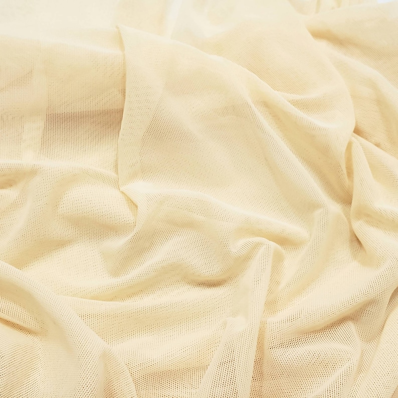 Pu&ograve; includere: Un primo piano di un tessuto color crema, trasparente, con una trama tessuta. Il tessuto &egrave; drappeggiato e piegato, creando linee morbide e fluide.