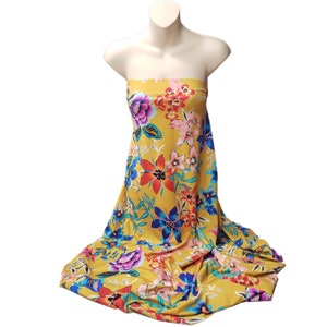 May include: A yellow fabric with a large floral print in shades of blue, red, pink, and white. The fabric is draped over a mannequin.