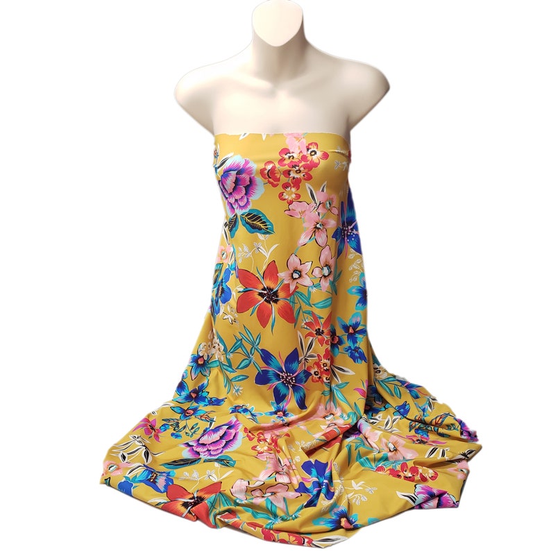 May include: A yellow fabric with a large floral print in shades of blue, red, pink, and white. The fabric is draped over a mannequin.