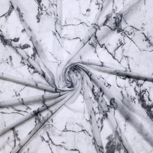May include: White and gray marble-patterned fabric. The fabric is a sheer mesh material with a swirling pattern. The gray veining creates a natural stone appearance. The fabric is folded and draped, showing the texture and design.