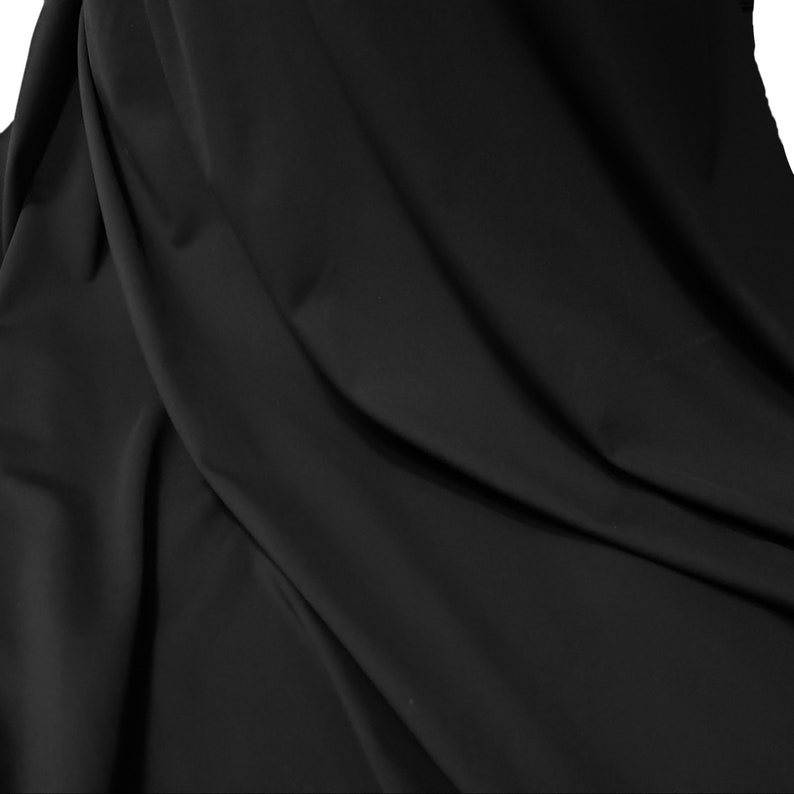 May include: A close-up shot of black fabric with soft folds and subtle shadows. The material appears smooth and opaque, with a slight sheen. The fabric is draped, creating a sense of depth and texture. The overall impression is of a luxurious textile.