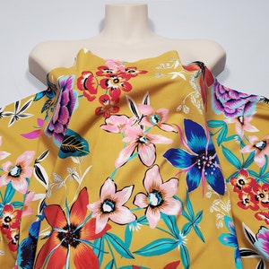 May include: Mustard yellow fabric with a floral print featuring pink, blue, red, and green flowers. The fabric has a soft, flowing texture.