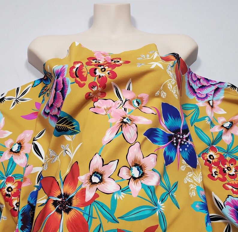 May include: Mustard yellow fabric with a floral print featuring pink, blue, red, and green flowers. The fabric has a soft, flowing texture.