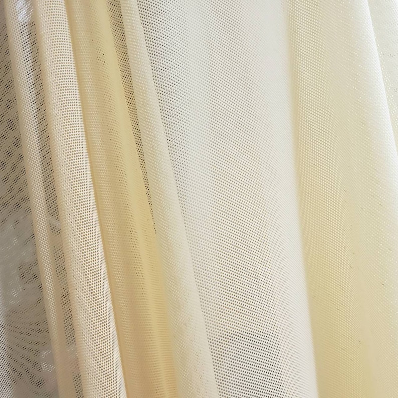 Pu&ograve; includere: Primo piano di un tessuto trasparente di colore giallo pallido con un fine motivo a rete. Il tessuto &egrave; drappeggiato e piegato, creando pieghe e grinze morbide.