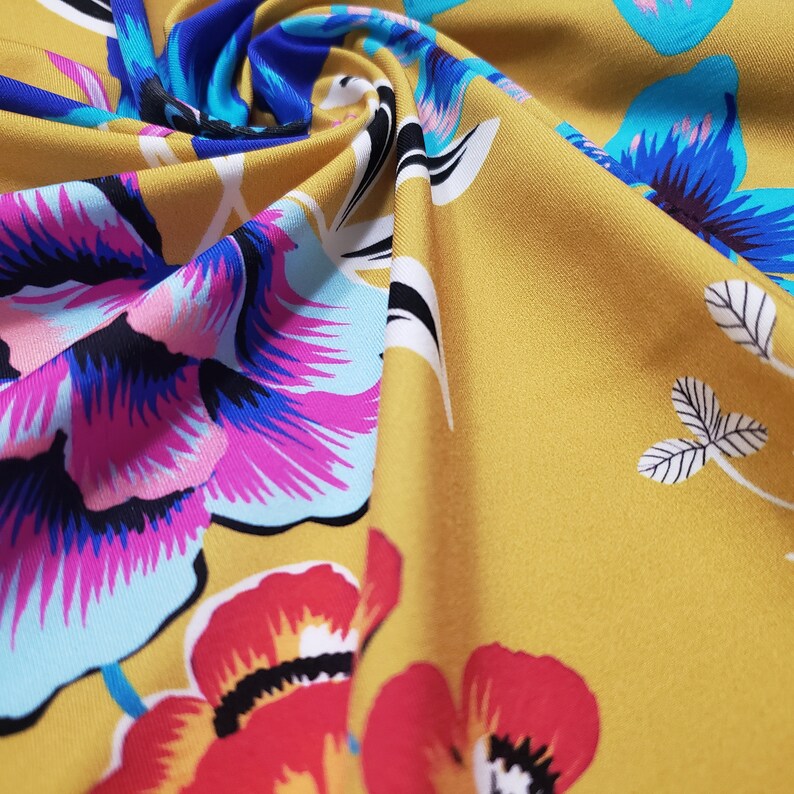 May include: A yellow fabric with a floral print featuring pink, blue, and red flowers. The fabric has a soft, silky texture.