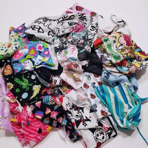 May include: A collection of patterned fabric pieces in a variety of colours. Designs include floral, cartoon characters, and abstract patterns. The fabrics are in shades of pink, black, white, blue, and green.