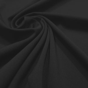 May include: A close-up shot of black fabric with a soft, flowing texture. The material is draped and swirled, creating a pattern of shadows and highlights. The fabric appears to be a solid color, with no visible patterns or designs.