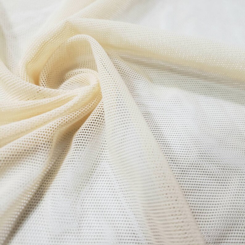 Pu&ograve; includere: Primo piano di un tessuto a rete color crema con una trama fine e uniforme. Il tessuto &egrave; morbido e flessibile, con una superficie leggermente strutturata.