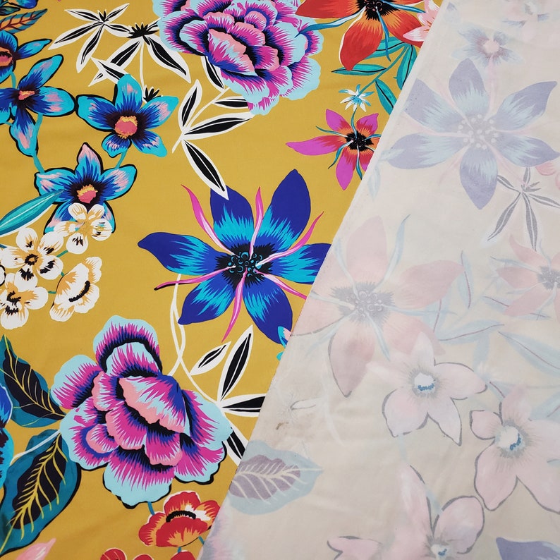 May include: A yellow fabric with a floral pattern. The fabric features large pink, blue, and red flowers with green leaves. The fabric is layered over a white fabric with a floral pattern.