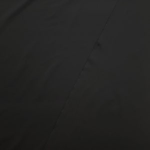 May include: A solid black fabric with a diagonal seam running across the image. The fabric appears to be smooth and possibly a garment material. The image is a close-up, focusing on the texture and color of the textile.