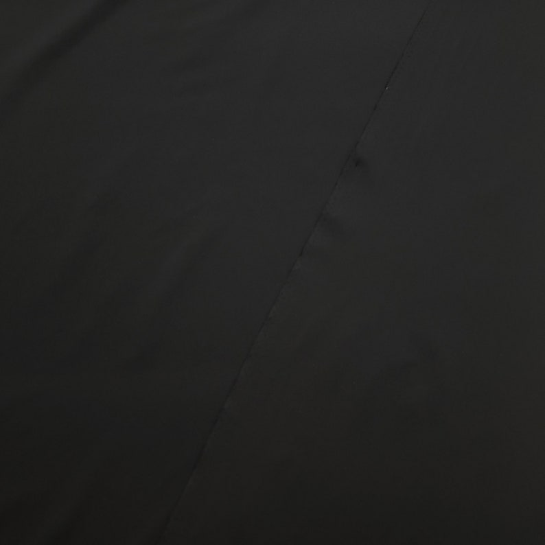 May include: A solid black fabric with a diagonal seam running across the image. The fabric appears to be smooth and possibly a garment material. The image is a close-up, focusing on the texture and color of the textile.