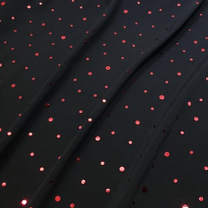 May include: Black fabric with scattered red polka dots. The fabric is draped, showing folds and shadows. The red dots vary in size and are evenly spaced across the material.