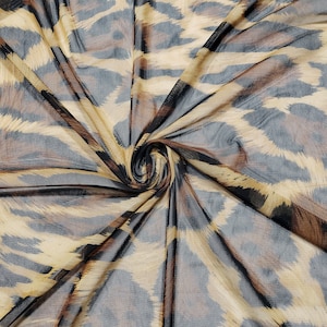 Puede incluir: Una tela transparente con un estampado de leopardo marrón y negro. La tela está drapeada y retorcida, mostrando la textura del material.